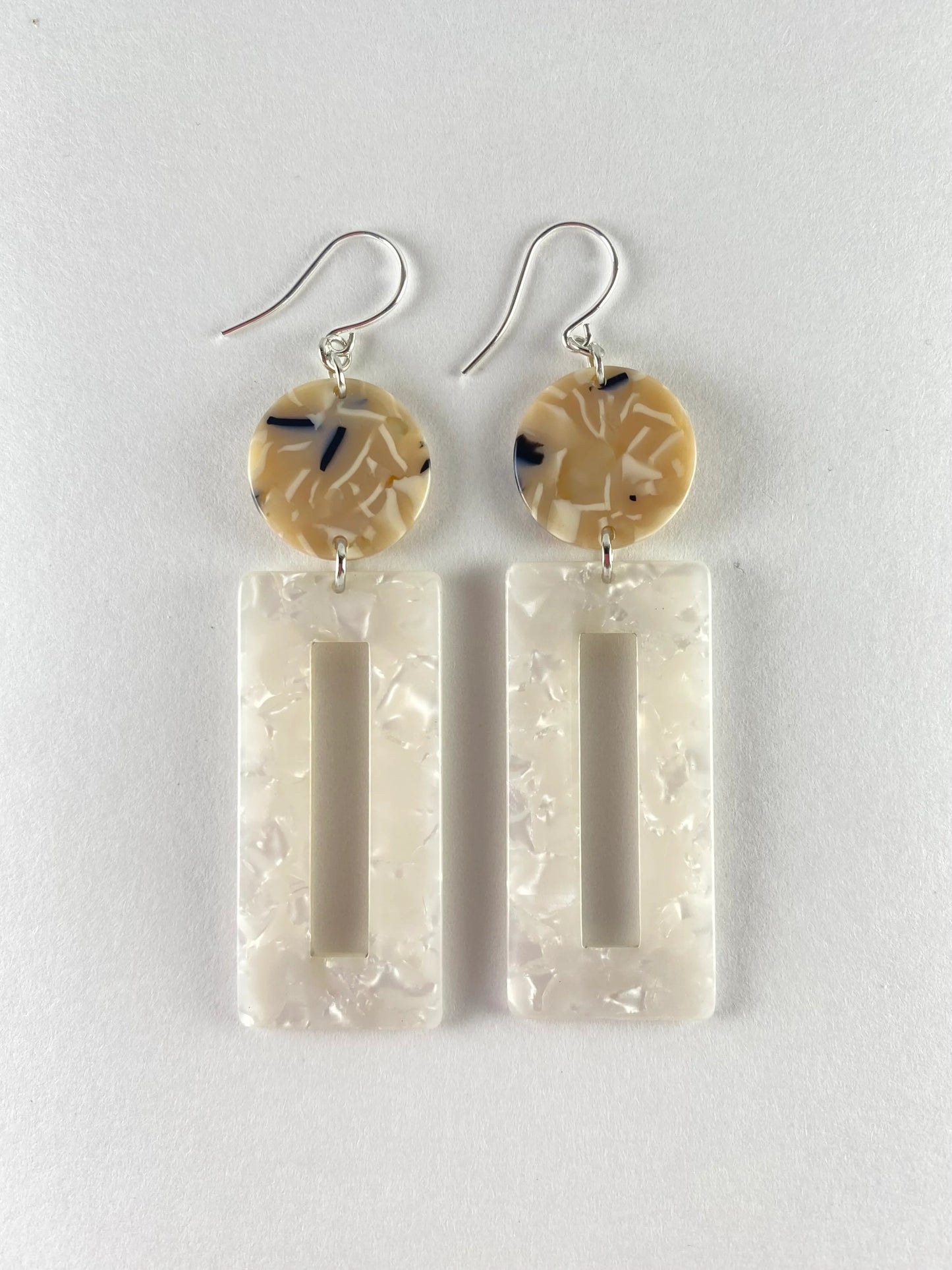 Dangling earring with 2 geometric beads. One a dime sized marble midnight blue, beige and white bead with a large pearl white rectangle shaped donut bead.