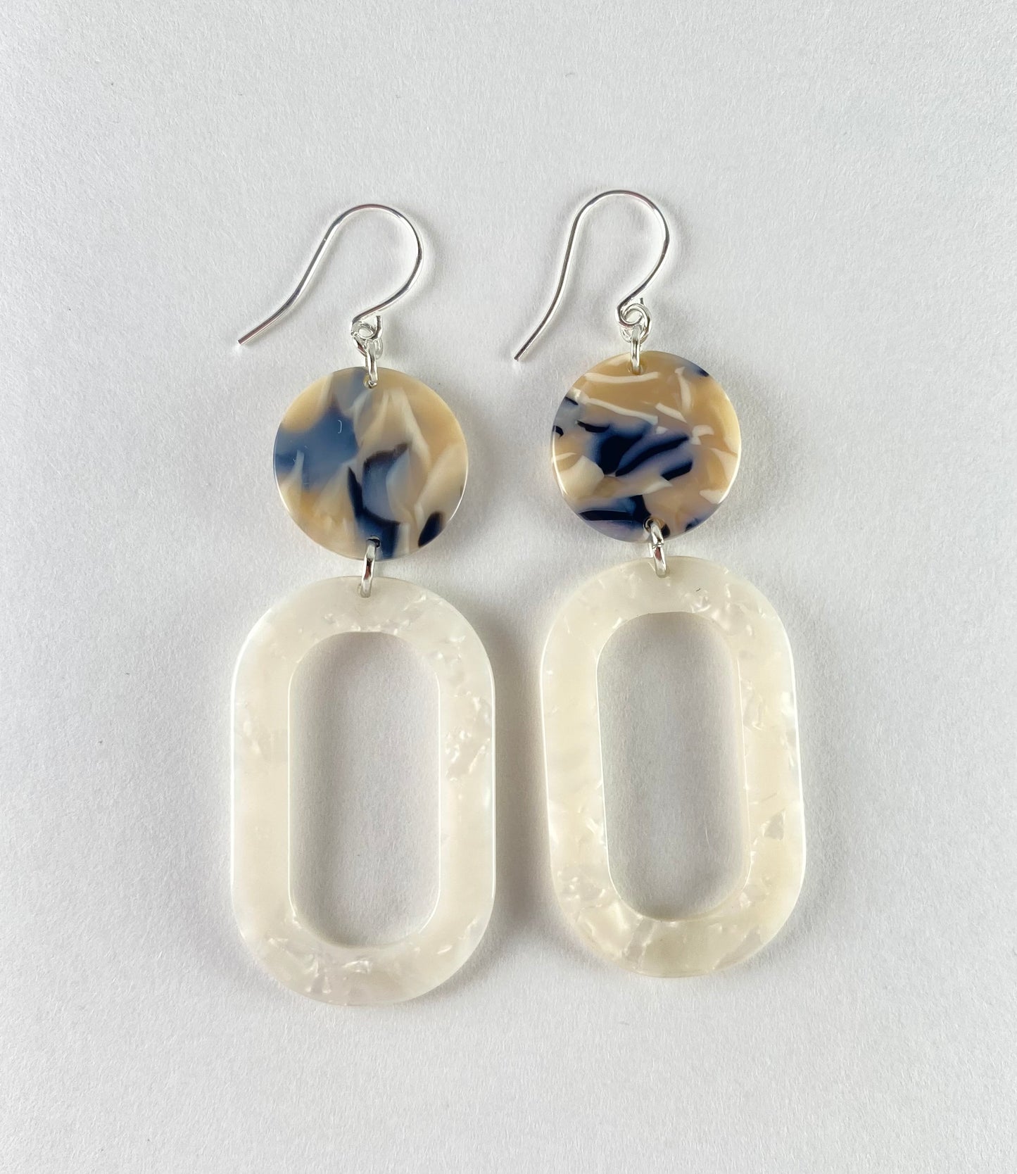 Dangling earring with 2 geometric shaped beads. 1 marbled disc is midnight blue with white and beige connected to 1 white oval donut.