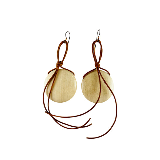 Dangling earring with blond wooden disk attached with copper colored leather cord.
