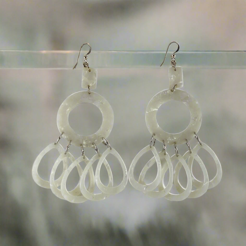 Dangling earring in pearl white components.  There is a small rectangle, an open donut and five individual teardrops.
