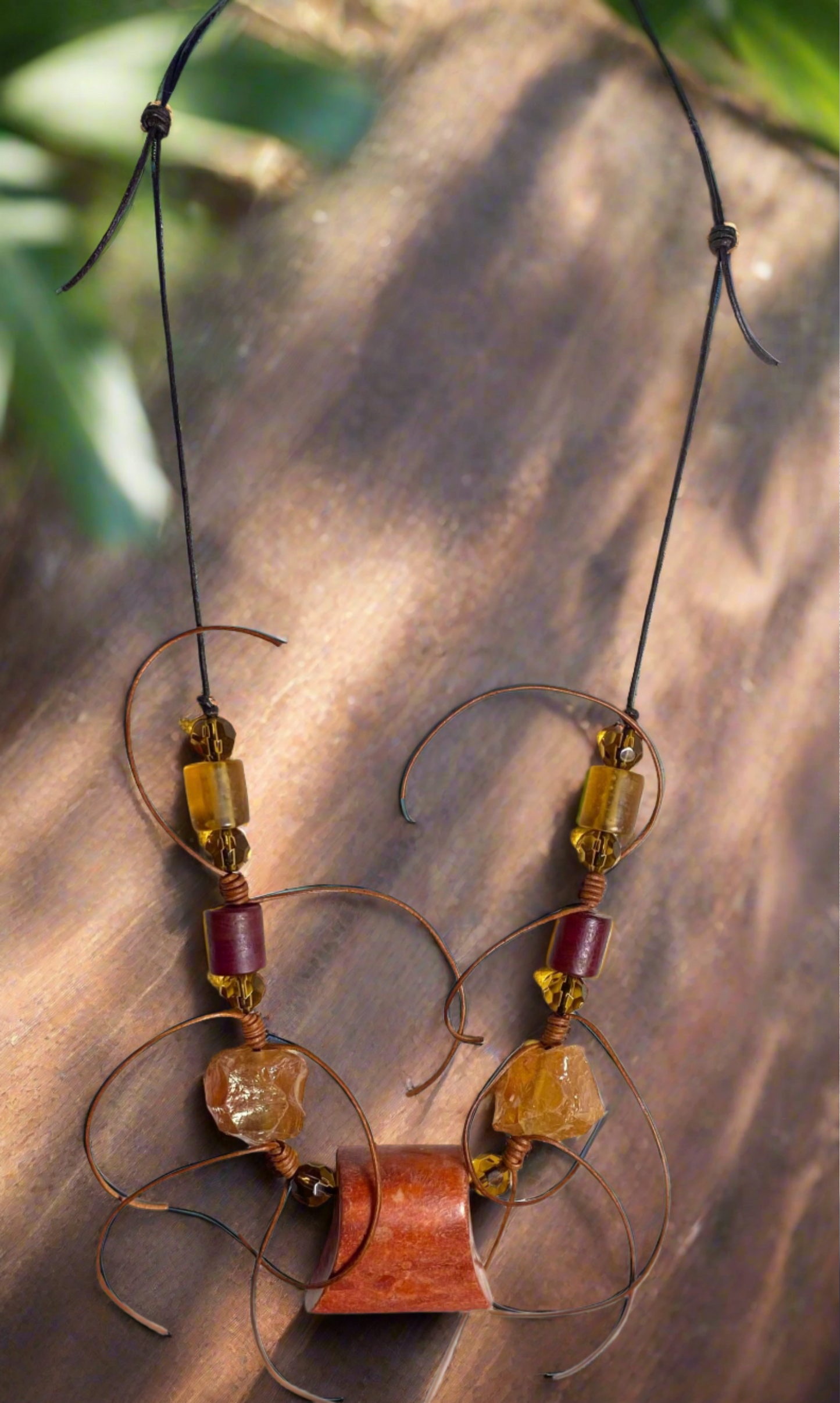 Orange trapazoid focal bead accented with large 1 inch rough cut light orange beads, burgundy and amber barrel shaped beads and small round faceted amber beads with loose ended barrel knots. Necklace has adjustable length.
